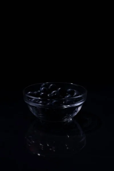En handfull blåbär i en glasskål på svart bakgrund — Stockfoto