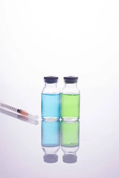 Detailní vakcína. Skleněné injekční lahvičky s vícebarevnou tekutinou a injekční stříkačkou na bílém pozadí. — Stock fotografie