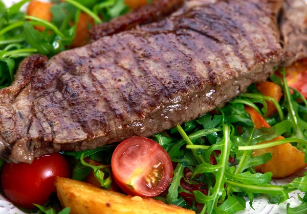 Cerca de filete de res rara con patatas asadas, tomates y hojas de cohete silvestres . — Foto de Stock