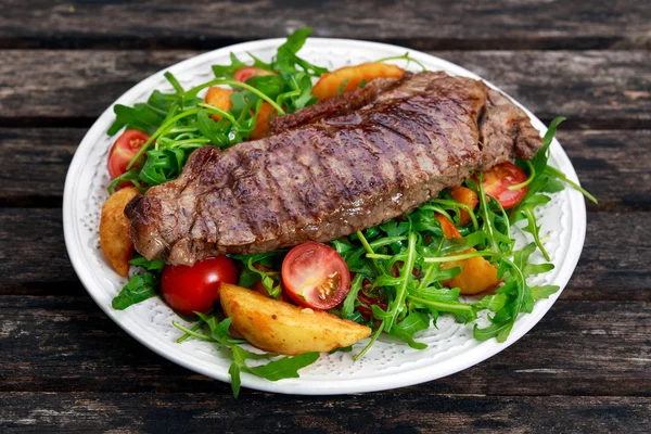 Hovězí steak s pečenými bramborami, rajčaty a rukola listy. — Stock fotografie