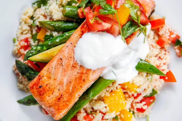 Pan fried Salmon with tender asparagus, courgette served on couscous mixed with sweet tomato, yellow pepper, with greek yogurt — Stock Photo, Image