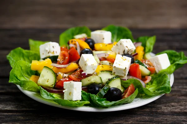 Φρέσκο λαχανικό ελληνική σαλάτα με τυρί φέτα, μαύρες ελιές, λάδι ελιές, ντοματίνια, κίτρινο πιπέρι, κόκκινο κρεμμύδι, αγγούρι. Στο ξύλινο τραπέζι. — Φωτογραφία Αρχείου