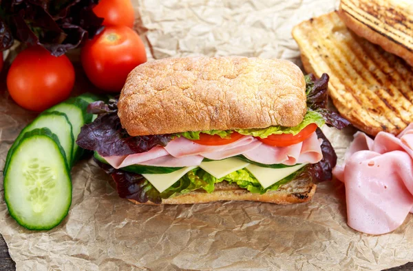 Sanduíche grelhado com alface, fatias de tomate fresco, pepino, cebola vermelha, salame, presunto e queijo . — Fotografia de Stock