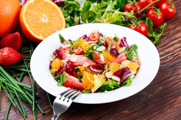 Salát z čerstvé zeleniny oranžový, jahoda. na dřevěný stůl. — Stock fotografie