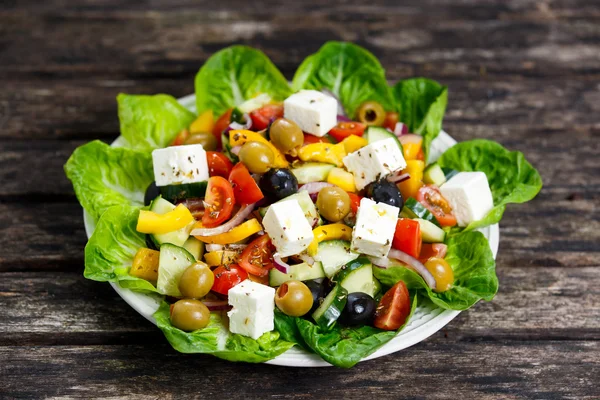 Insalata greca di verdure fresche con formaggio Feta, olive verdi nere, olio d'oliva. pomodorini, peperone giallo, cipolla rossa, cetriolo. Su tavolo di legno . — Foto Stock