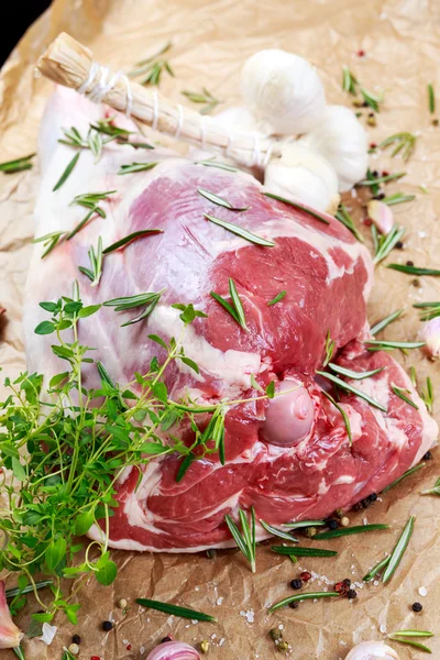 Jambe d'agneau cru sur fond de papier froissé avec des herbes — Photo