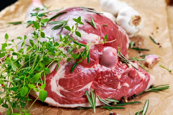 Jambe d'agneau cru sur fond de papier froissé avec des herbes — Photo