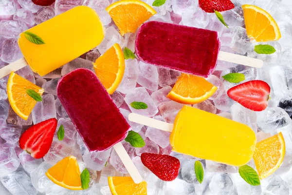 Osvěžující ovocné popsicle lízátka na ledu pozadí s plody, máta. — Stock fotografie
