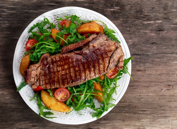 Vzácné hovězí steak s pečenými brambory, rajčata, rukola listy. — Stock fotografie