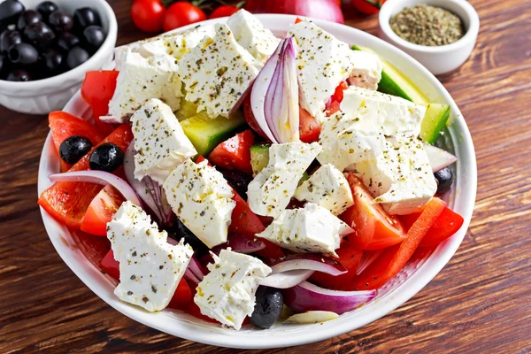 Ensalada griega con pimiento dulce fresco, cebolla roja, tomates cherry de naranja, pepino, aceitunas negras y queso feta rociado aceite de oliva virgen extra sobre mesa de madera —  Fotos de Stock