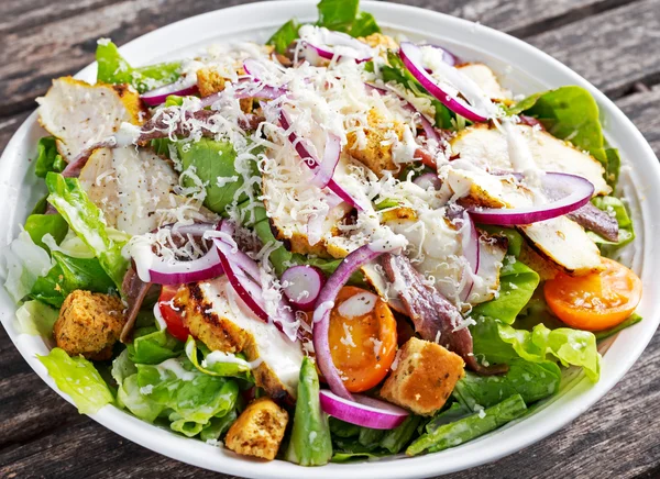 Ensalada de Ceasar con filetes de pollo a la parrilla, aros de cebolla roja, lechuga, tomates cherry de naranja, croutons, queso parmesano rallado, anchoa sazonada —  Fotos de Stock