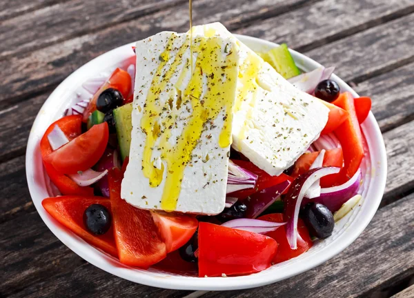 Ensalada griega con pimiento dulce fresco, cebolla roja, tomates cherry de naranja, pepino, aceitunas negras y queso feta rociado aceite de oliva virgen extra sobre mesa de madera —  Fotos de Stock