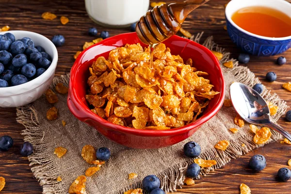 Corn Flakes with berries raspberries, blueberries, glass of milk, and sweet honey.