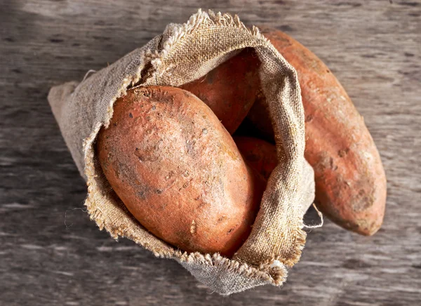 Batatas-doces orgânicas recém-colhidas em um saco de serapilheira na mesa de madeira . — Fotografia de Stock