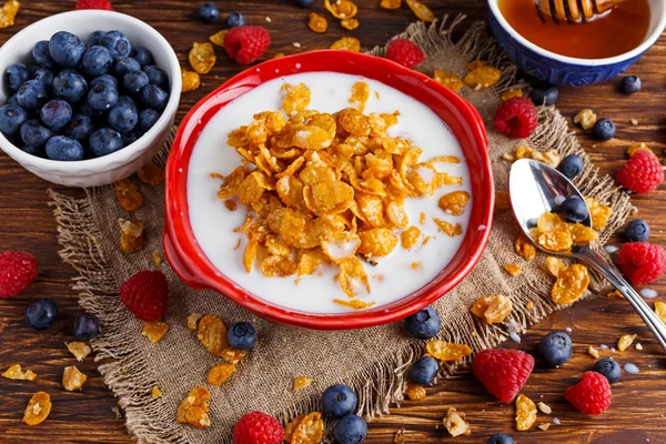 Corn Flakes with berries raspberries, blueberries, glass of milk, and sweet honey. — Stock Photo, Image