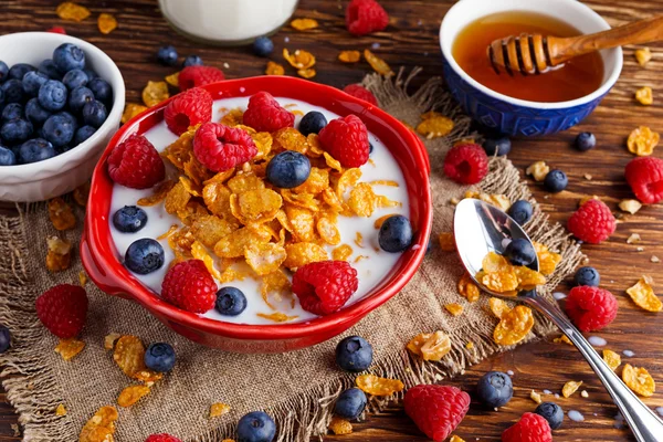 Corn Flakes with berries raspberries, blueberries, glass of milk, and sweet honey. — Stock Photo, Image