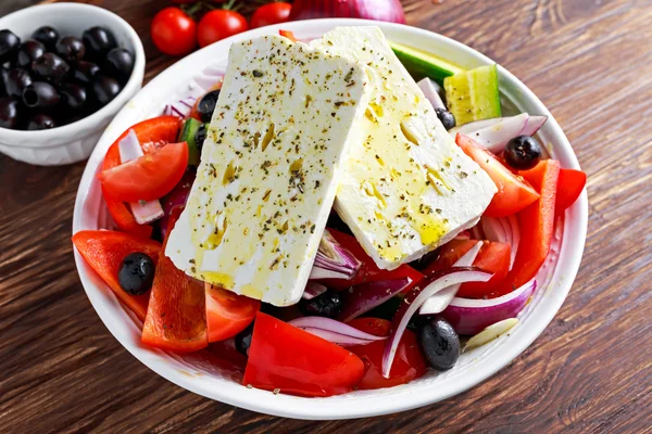 Görög saláta friss paprika, lilahagyma, narancs, cseresznye paradicsom, uborka, fekete olajbogyó és feta sajtot drizzled, extra szűz olívaolaj, a fából készült asztal — Stock Fotó