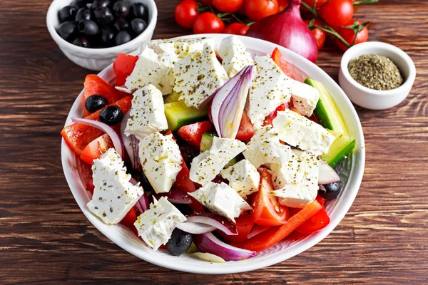 Griekse salade met verse paprika, rode ui, oranje cherry tomaten, komkommer, zwarte olijven en feta kaas besprenkeld extravergine olijfolie op houten tafel — Stockfoto