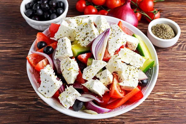 Ensalada griega con pimiento dulce fresco, cebolla roja, tomates cherry de naranja, pepino, aceitunas negras y queso feta rociado aceite de oliva virgen extra sobre mesa de madera —  Fotos de Stock