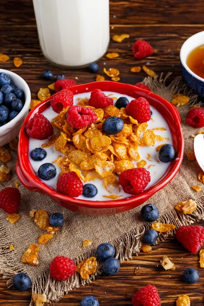 Corn Flakes with berries raspberries, blueberries, glass of milk, and sweet honey.