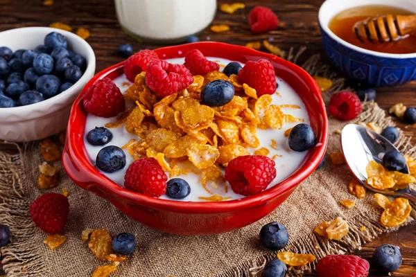 Corn Flakes with berries raspberries, blueberries, glass of milk, and sweet honey. — Stock Photo, Image