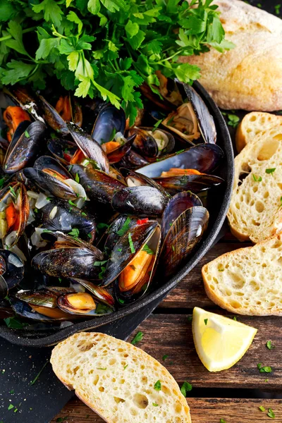 Mejillones hervidos en un plato de hierro para cocinar. con hierbas, mantequilla, lima, perejil, ajo y pan fresco . — Foto de Stock