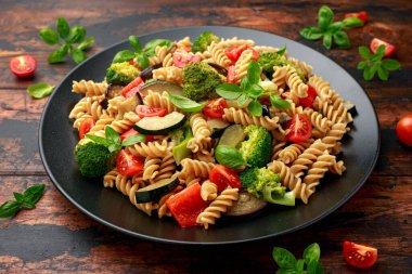 Sebzeli Fusilli makarna, brokoli, kabak, kırmızı biber, patlıcan, domates ve siyah tabakta fesleğen.