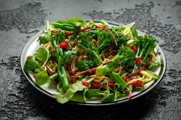 Tenderstem broccoli and egg noodles Азіатський вегетаріанський салат з смаженим сосновим горіхом і насінням граната. — стокове фото