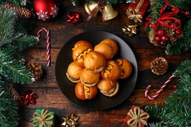 Noel mini hamburgerleri, hamburger ve sosisli sandviç. Süslü, hediyeli, ahşap kırsal masada yeşil ağaç dalı.