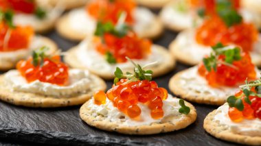 Somon havyarı ve yumuşak peynirli tuzlu kraker. Siyah tahta üzerinde susam ve haşhaş tohumlu.