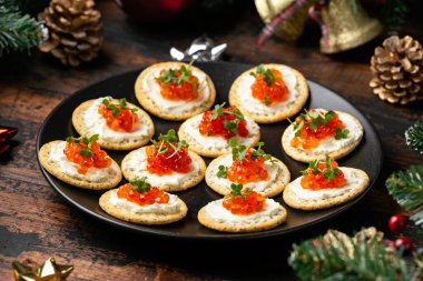 Somon havyarı ve yumuşak peynirli kraker süslemeli, hediyeli, yeşil ağaç dallı ahşap masa..