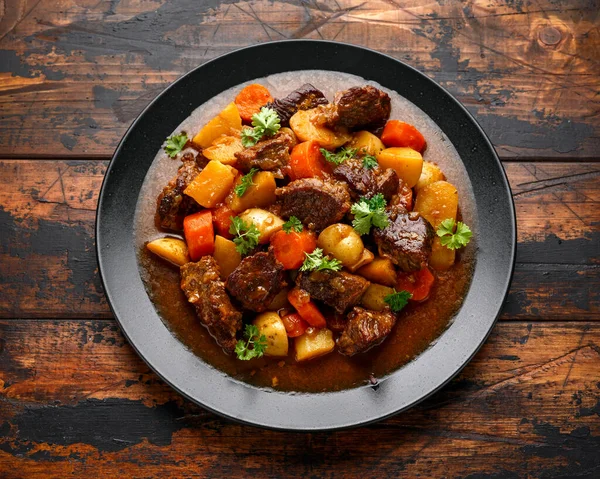 Beef Stew with carrot and baby potato in black plate on wooden table — Stock Photo, Image