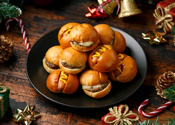 Christmas mini hamburgers, burger and hot dogs with decoration, gifts, green tree branch on wooden rustic table — Stock Photo, Image