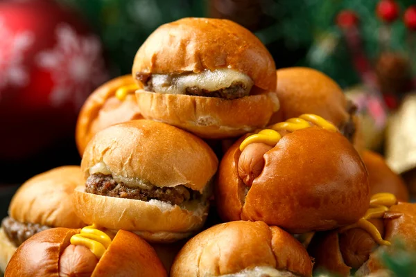 Mini hamburguesas de Navidad, hamburguesas y perritos calientes con decoración, regalos, rama de árbol verde en mesa rústica de madera —  Fotos de Stock