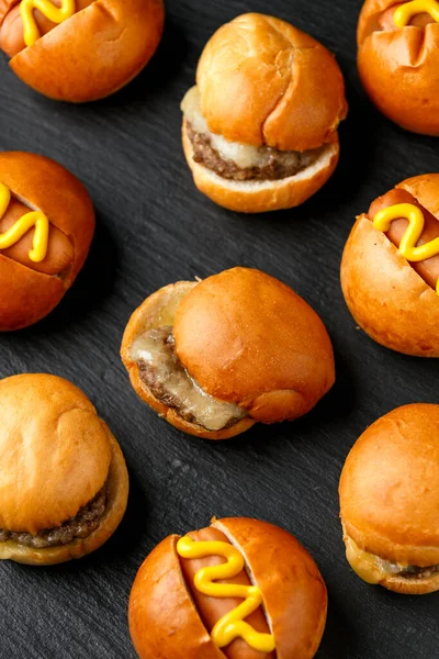 Mini hamburgers, burger and hot dogs with yellow mustard on black slate board — Stock Photo, Image