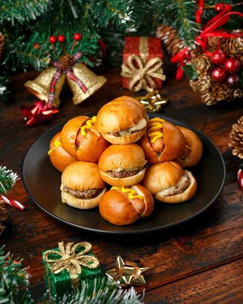 Mini hamburguesas de Navidad, hamburguesas y perritos calientes con decoración, regalos, rama de árbol verde en mesa rústica de madera —  Fotos de Stock