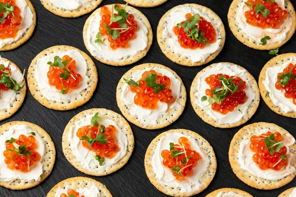 Caviar de salmón y galletas saladas de queso blando con semillas de sésamo y amapola servidas en pizarra negra —  Fotos de Stock