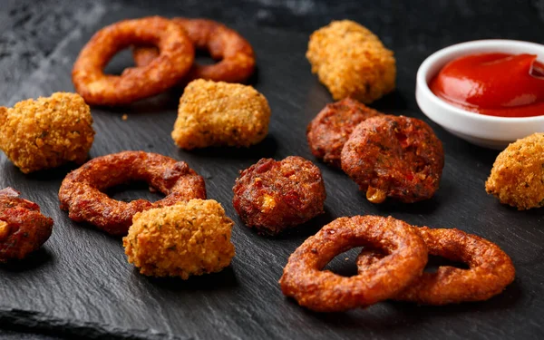 Stekt buffel lökringar, tater tots och sockermajs frittrar med ketchup på rustika stenskivor. Festen tar bort mat — Stockfoto