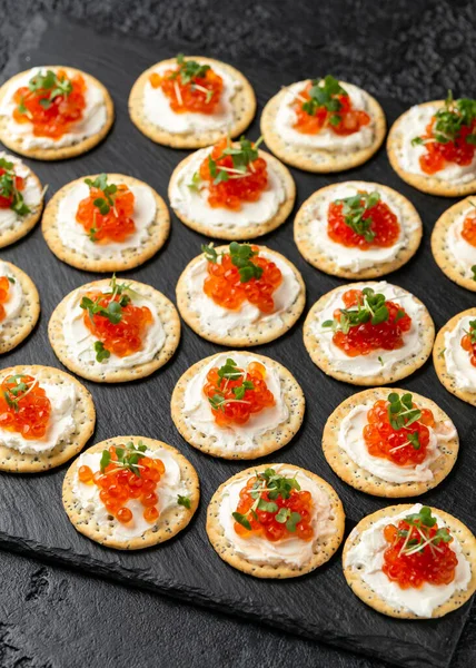 Caviar de salmão e bolachas salgadas de queijo mole com gergelim e sementes de papoula servidas em tábua de ardósia preta — Fotografia de Stock