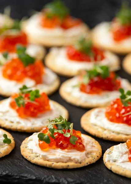 Caviar de salmón y galletas saladas de queso blando con semillas de sésamo y amapola servidas en pizarra negra —  Fotos de Stock