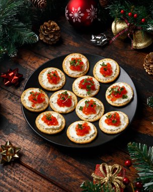 Somon havyarı ve yumuşak peynirli kraker süslemeli, hediyeli, yeşil ağaç dallı ahşap masa..