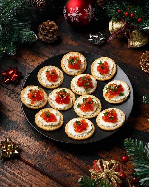 Salmon caviar and soft cheese savory crackers with decoration, gifts, green tree branch on wooden rustic table. — Stock Photo, Image