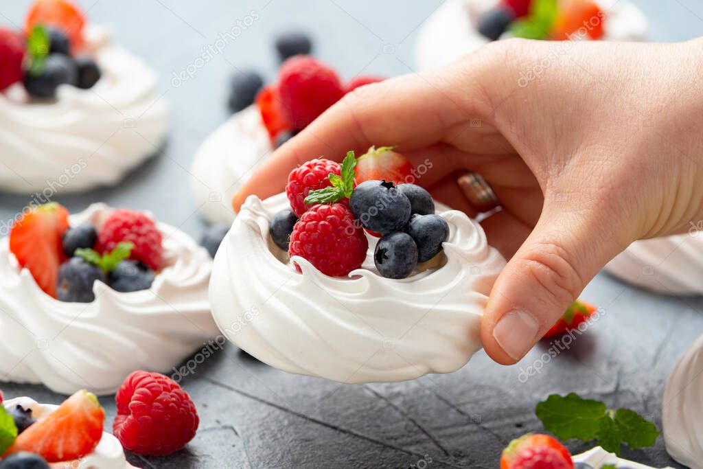 Woman's Hand pick up meringue nest mini pavlova cake with fresh berries strawberry blueberry raspberry and mint for healthy desert.