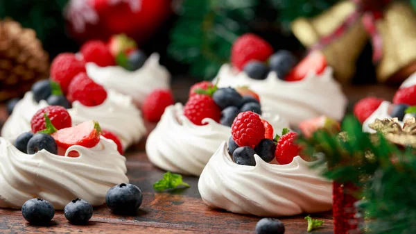 Meringue häckar mini pavlova kakor med färska bär jordgubbe blåbär hallon och mynta för middag öken med julen festliga dekorationer — Stockfoto