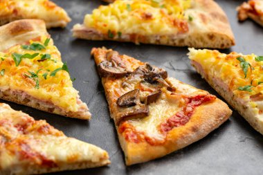 Siyah masa üzerinde farklı malzemelerle dilimler halinde pizza.