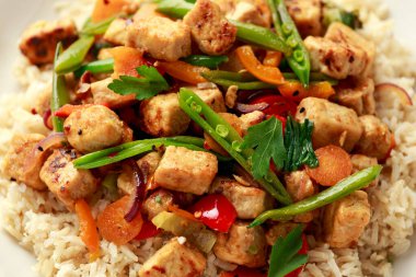 Vejetaryen etsiz micoprotein parçaları sebze kızartması, beyaz tabakta servis edilen kahverengi pirinç.