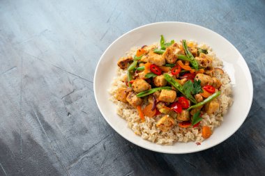 Vejetaryen etsiz micoprotein parçaları sebze kızartması, beyaz tabakta servis edilen kahverengi pirinç.