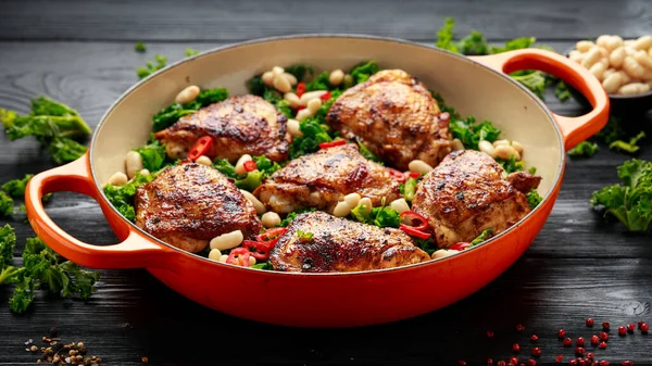 One-pot braised chicken thighs with kale and cannellini beans served with chili peppers.