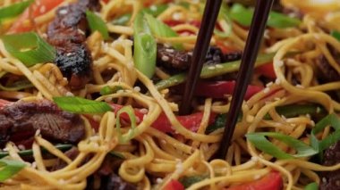 Yemek çubuğu kullanarak kaseden sığır eti ve sebzeli erişte topluyorum. Asya tarzı yemekler..