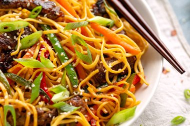 Kızarmış erişteyi sığır eti ve sebzeyle karıştırın. Asya usulü yemek.